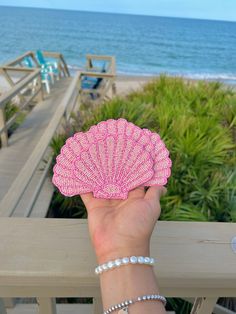 a hand holding a pink fan on top of a wooden deck next to the ocean