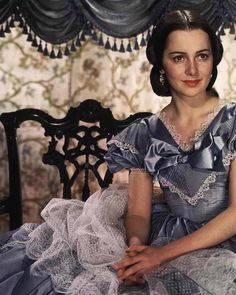 a woman sitting on top of a bed in a blue dress with ruffles