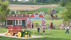 children are standing in front of a red and green barn with a train on it