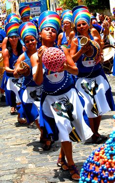 a group of women dressed in blue and white dresses holding items while standing on the street