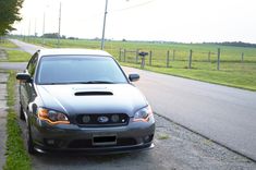 a silver car parked on the side of a road next to a grass covered field