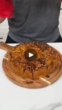 a man standing in front of a cake on top of a wooden cutting board with pecans