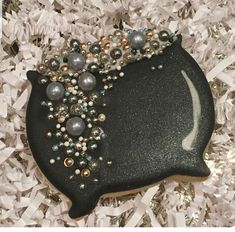 a black and silver decorated cookie sitting on top of white shredded paper with beads around it