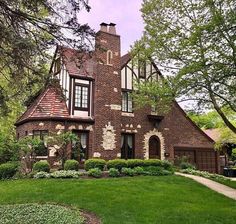 a large brick house in the middle of a green yard with lots of trees and bushes