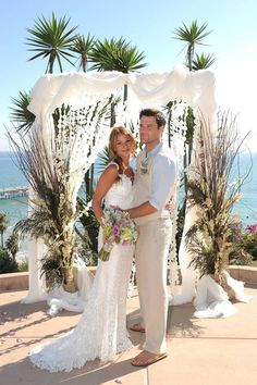 a bride and groom pose for a photo in front of an outdoor wedding ceremony arch