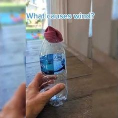 a hand is holding a plastic bottle with water in it that says, what cause wind?