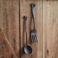 an old fork and spoon hanging on the side of a wooden wall next to a pair of tongs