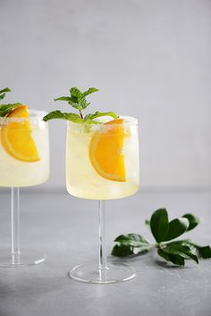 two cocktails with orange slices and mint garnish