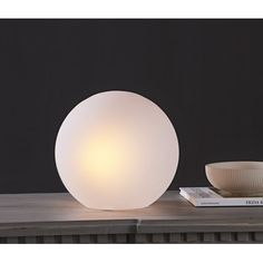 a white light sitting on top of a wooden table next to a bowl and book