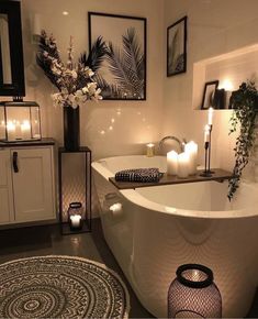 a white bath tub sitting in a bathroom next to candles and pictures on the wall