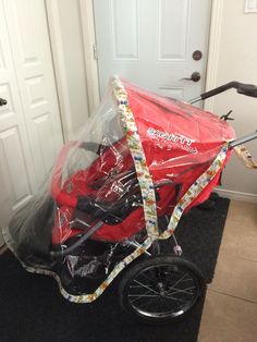 a red baby stroller covered in plastic sitting on the floor next to a door