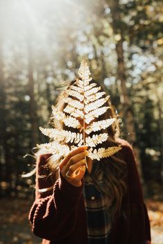 a woman holding a leaf in front of her face with the sun shining through it