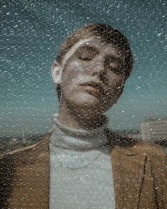 a man is looking out the window while wearing a brown jacket and white turtle neck sweater