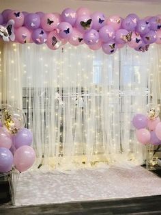 balloons and streamers are hanging from the ceiling in front of a window with sheer curtains