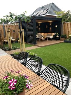 an outdoor living area with wooden tables, chairs and potted plants on the grass