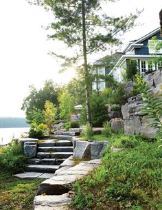 stone steps lead up to a house near the water's edge with trees and bushes