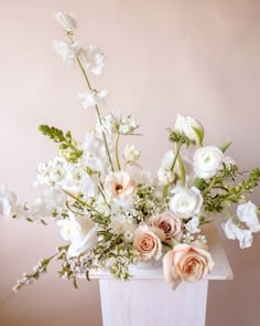 a white vase filled with lots of flowers on top of a wooden table next to a pink wall