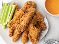 fried chicken sticks and celery on a white plate next to a bowl of dipping sauce