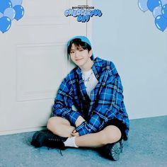 a boy sitting on the floor in front of a door wearing a blue hat and plaid shirt