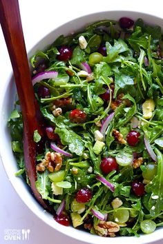 a white bowl filled with greens and cranberries on top of a table next to a wooden spoon