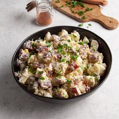 a black bowl filled with potato salad next to a cutting board and wooden utensils