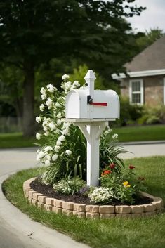 a white mailbox sitting in the middle of a flower bed next to a house