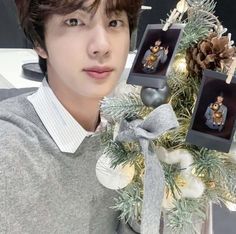 a young man wearing a sweater and bow tie next to a christmas tree with ornaments on it