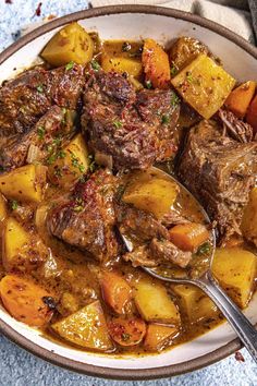 a bowl filled with stew and potatoes on top of a blue table cloth next to a spoon