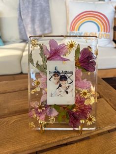 a photo frame with flowers and leaves in it sitting on a table next to a couch