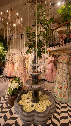 a room filled with lots of dresses hanging from the ceiling next to a fountain and potted plants