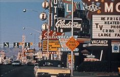 an old car is driving down the street in front of many signs and advertisements on buildings