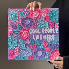 a woman holding up a card that says cool people live here with flowers on it