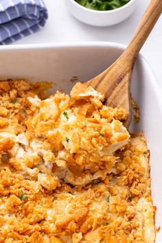 a casserole dish with chicken and cheese in it next to a bowl of greens