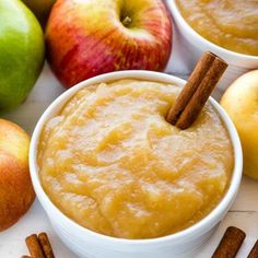 apples and cinnamon sticks sit next to two bowls of apple cider sauce on a white surface