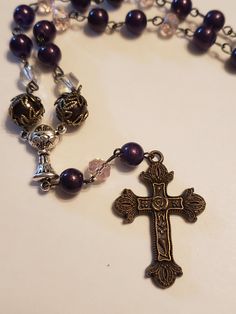 Rich dark purple glass beads make up this rosary. Light pink and clear crystals are placed throughout to highlight the beauty of the purple. Dark purple accent beads featuring bronze filigree bead caps add to the stunning piece. The focal point is the bronze decorative cross which completes the rosary gracefully. Decorative Cross, Bead Rosary, Purple Dark, Crosses Decor, Purple Accents, The Rosary, Clear Crystals, Purple Glass, Bead Caps