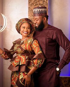 a man and woman dressed in traditional african clothing posing for a photo together with the lights on behind them