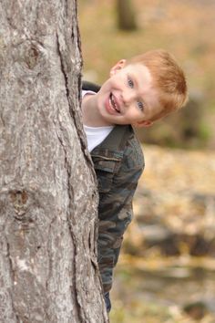 a young boy standing next to a tree