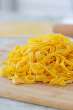 a pile of yellow noodles sitting on top of a wooden cutting board