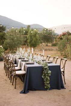 an outdoor dinner table set up with candles and greenery in the middle of it