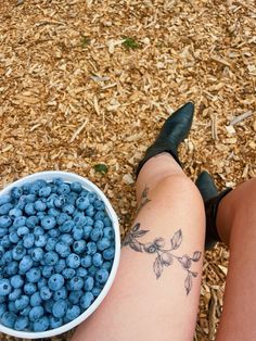 a woman sitting on the ground next to a bowl of blueberries with her legs crossed