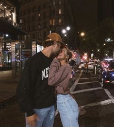 a man and woman standing next to each other on a street at night with cars passing by