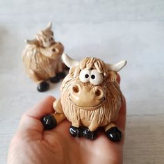 a hand holding a small toy cow with eyes and horns on it's head