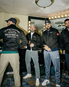 three men standing next to each other in front of a mirror with lights on it