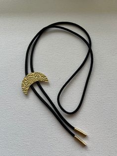 Bright yellow/gold brass crescent moon with floral pattern bolo tie necklace on black nylon cord. Adjustable Metal Lariat Necklace For Festivals, Handmade Adjustable Metal Lariat Necklace, Adjustable Crescent Brass Jewelry, Adjustable Handmade Metal Lariat Necklace, Adjustable Gold Lariat Necklace Choker, Adjustable Metal Crescent Necklace, Vintage Adjustable Moon Necklace, Adjustable Crescent Metal Necklace, Elegant Adjustable Crescent Jewelry