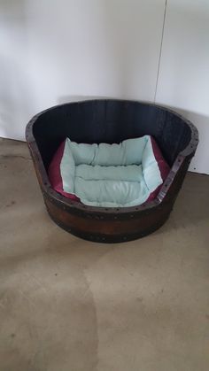 a dog bed made out of an old barrel is sitting on the floor in front of a white wall