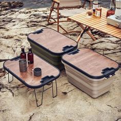 two coolers sitting on top of a rocky beach next to a picnic table and chairs