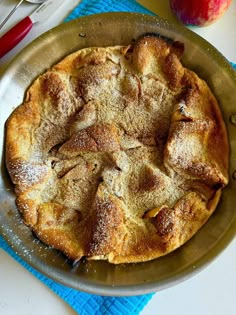 an apple pie with powdered sugar on top sits in a pan next to a knife and fork