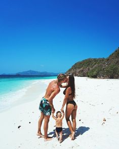 a man, woman and child are standing on the beach with blue water in the background