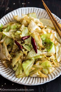 a white plate topped with cabbage and chopsticks next to a bowl of food