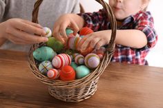 a young child is playing with an easter basket filled with colorfully painted plastic eggs